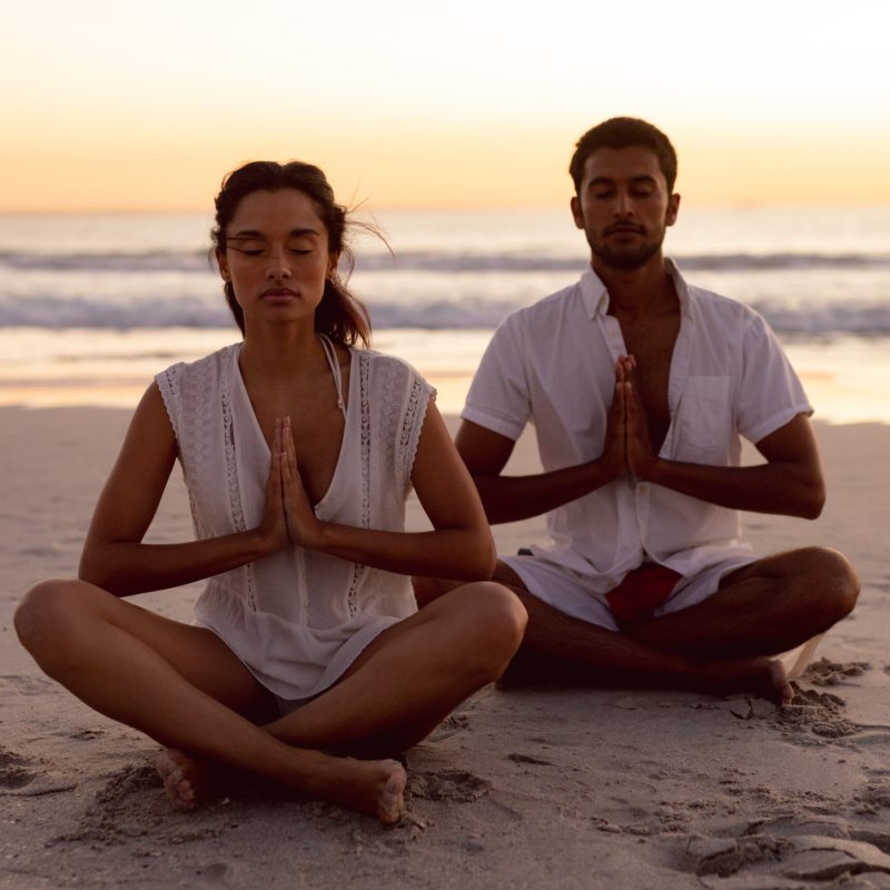 Couple performing yoga together on the beach during sunset